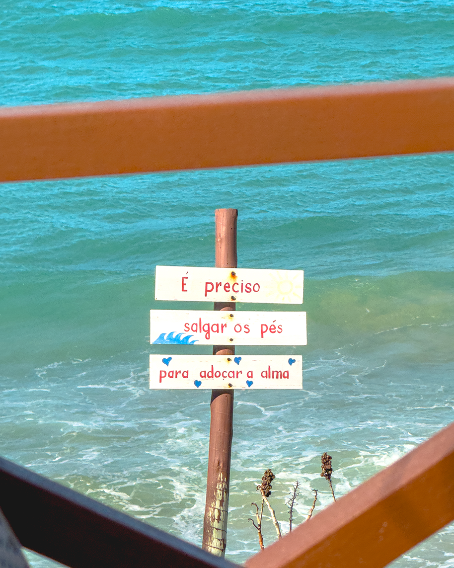 Placa de madeira indicando o caminho para o mar entre vegetação
